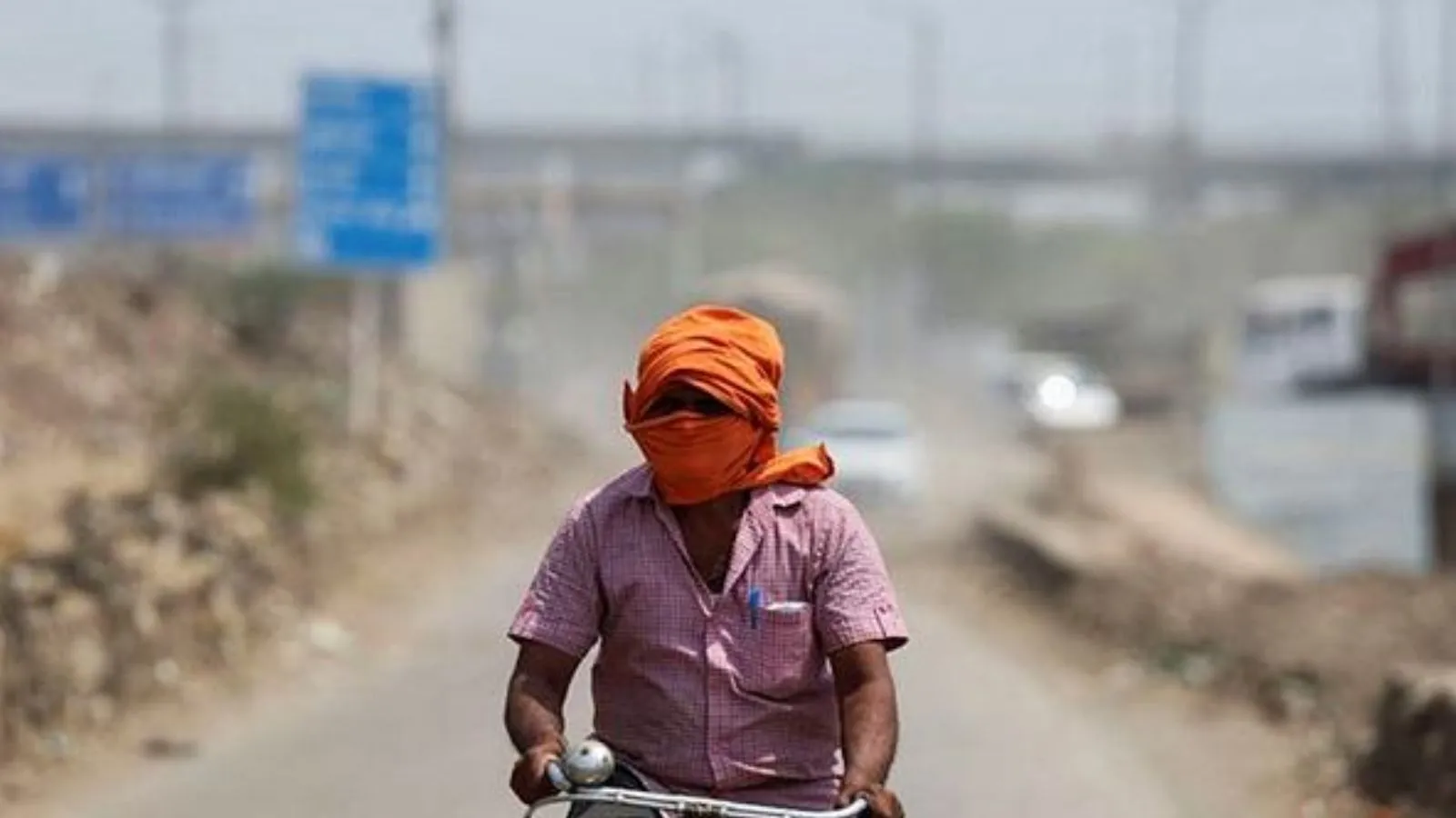 A man rides his cycle near a landfill site on a hot summer day during a heatwave in New Delhi,