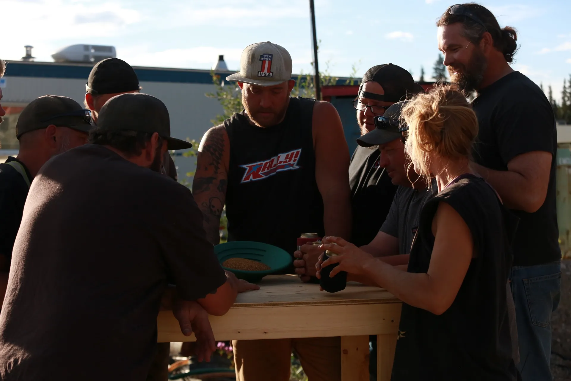 Ness crew gathering around table staring at gold in goldpan.