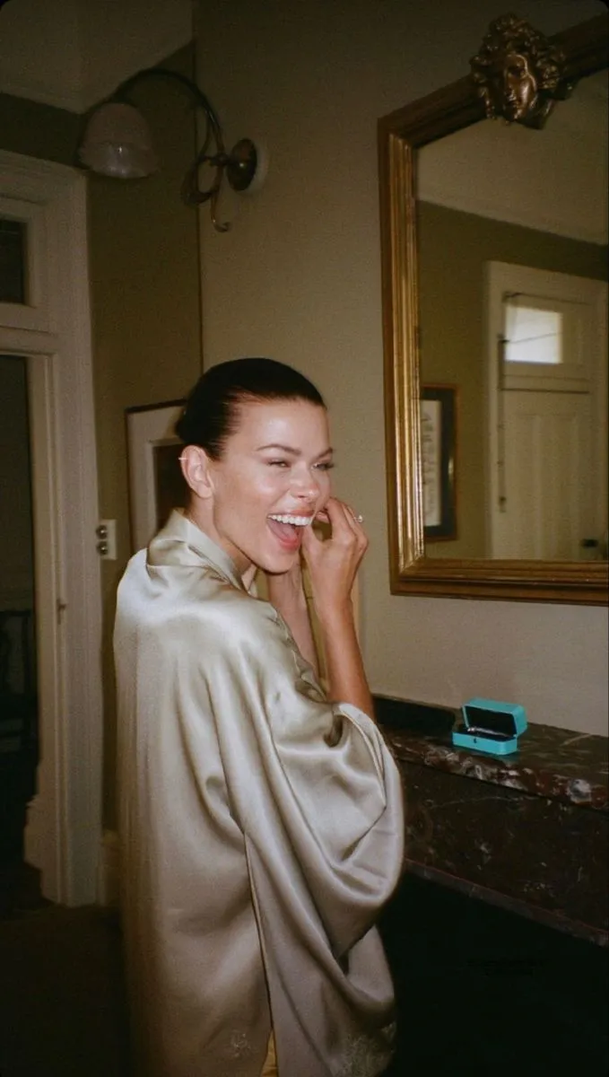 This may contain: a woman standing in front of a mirror talking on a cell phone while wearing a robe