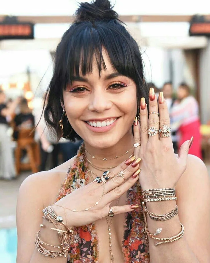 This may contain: a woman with lots of rings on her hand and wearing jewelry around her neck smiling at the camera
