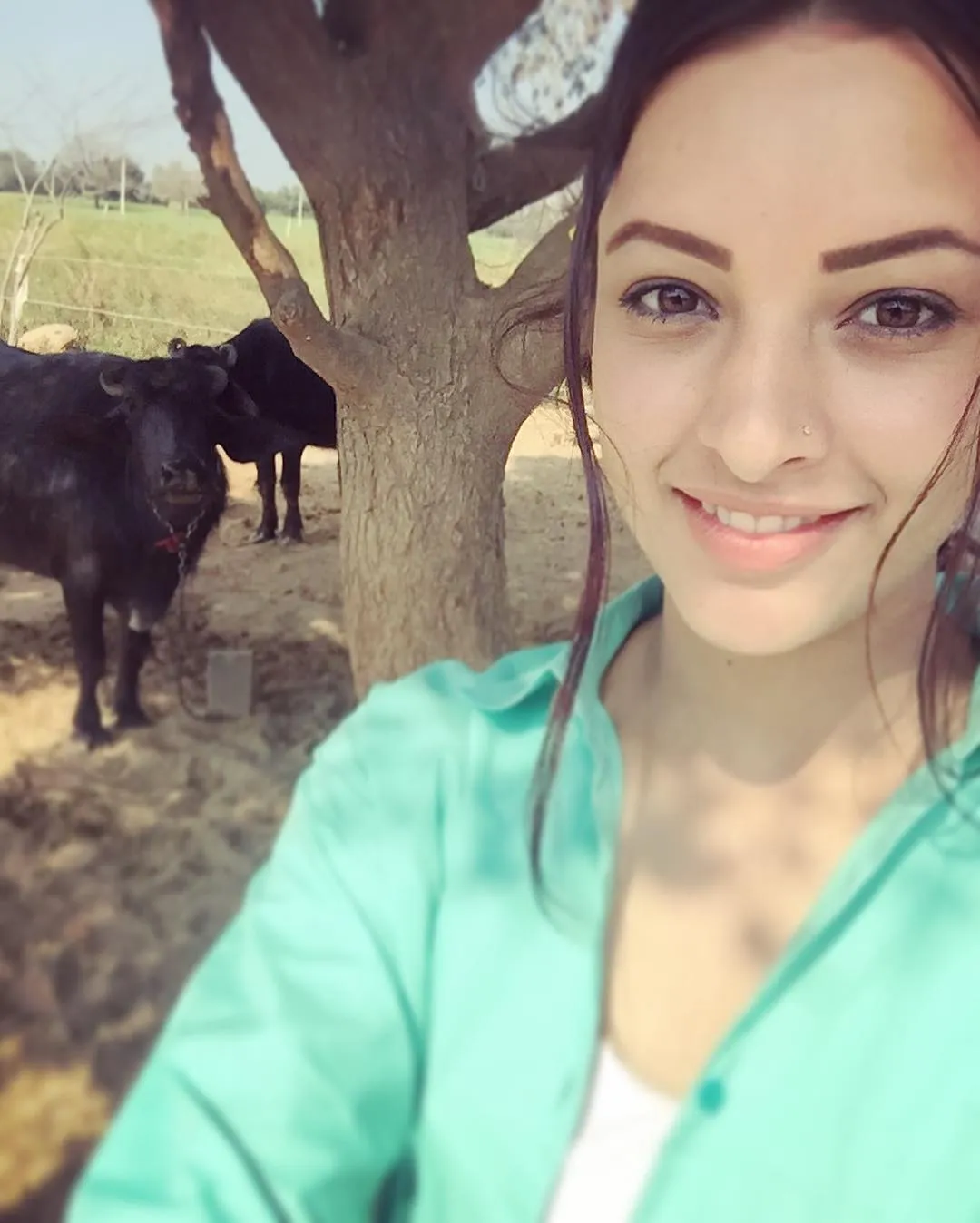 Tripti Dimri smiling while taking a selfie under a tree. In the background, there are buffaloes and a calm, open field, giving the photo a relaxed, countryside vibe. The image reflects her love for simple moments in na.jpg  