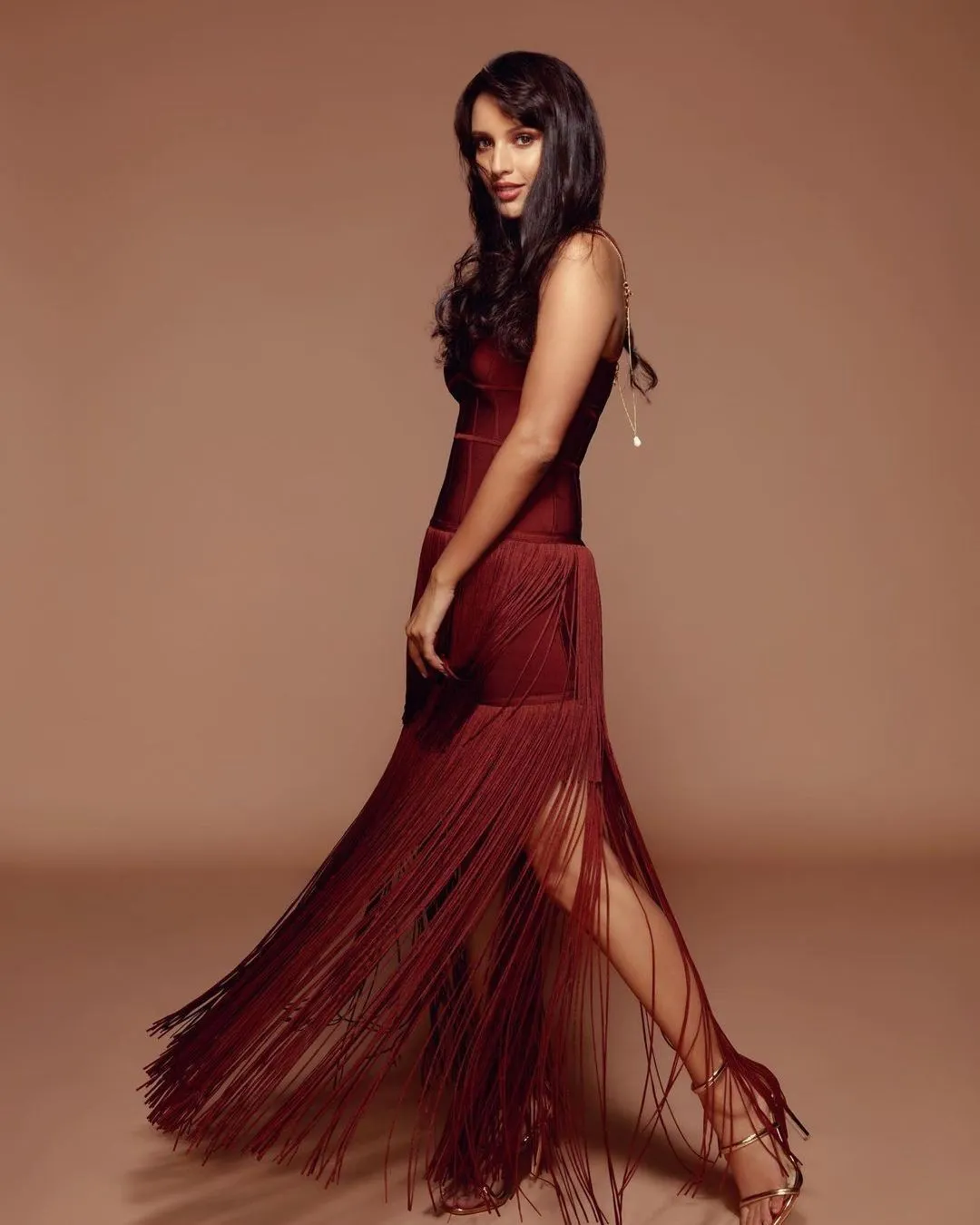 Tripti Dimri in a stylish maroon dress with long fringes. The dress fits her well at the top, and the fringes add a flowing effect. She is standing to the side, looking confidently at the camera, with her hair resting.jpg  
