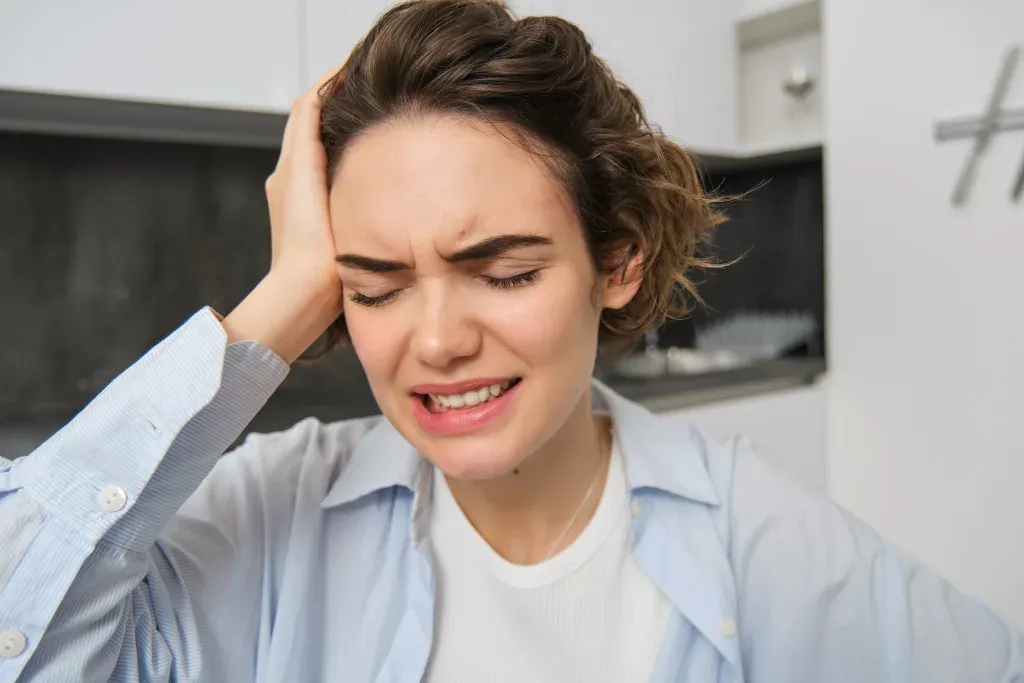 Portrait of brunette woman touches her head, grimaces from pain, has headache, painful migraine