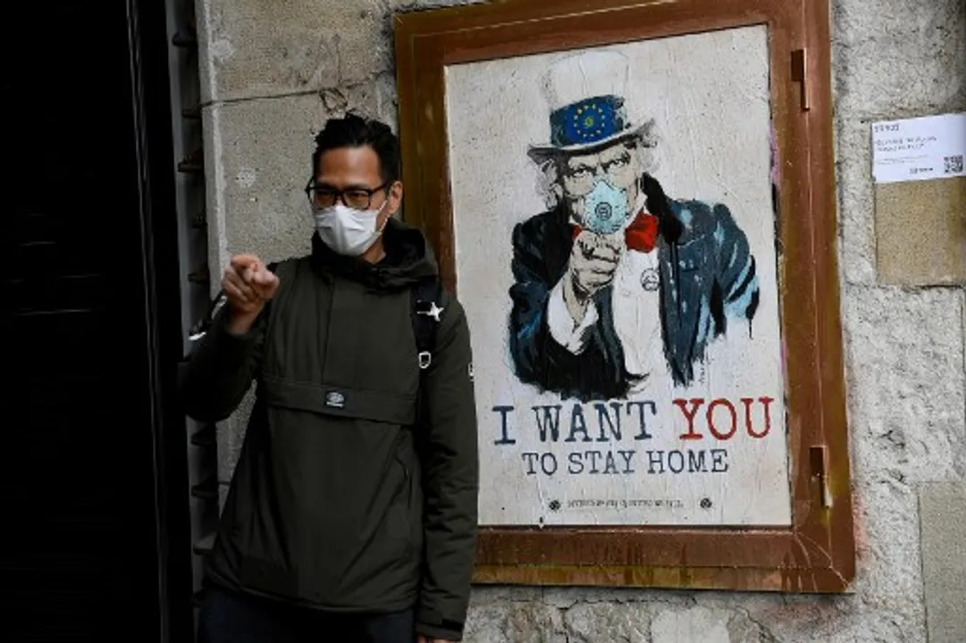  A man wearing a face mask poses with a poster by artist TVBoy featuring Uncle Sam and reading "I want you to stay home" in Barcelona Photograph:(AFP) 