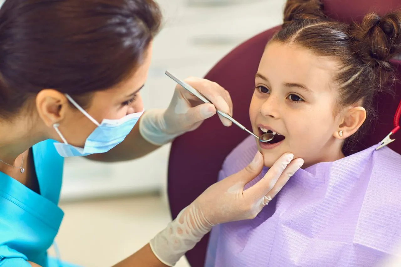 Woman Dentist Examining Smiling Child Girls Teeth with Mirror in Dental Clinic