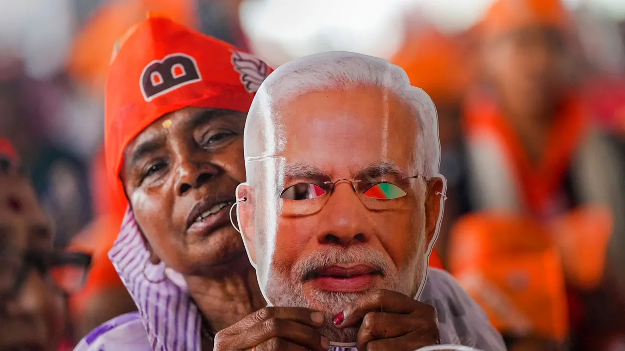 A BJP supporter holds a mask of Prime Minister Narendra Modi during his election campaign rally ahead of Lok Sabha polls, in Meerut, Sunday, March 31, 2024