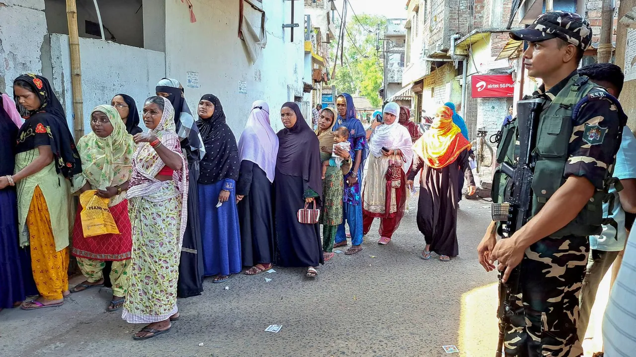 A security official stands guard as women wait in a queue to cast their vote at a polling station at Kharagpur, during the sixth phase of Lok Sabha elections, in Paschim Medinipur district, Saturday, May 25, 2024