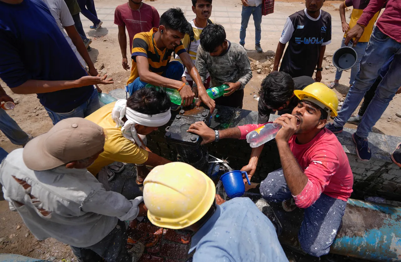 Workers collect drinking water from a leaking pipeline to quench their thirst during a hot summer afternoon, in New Delhi