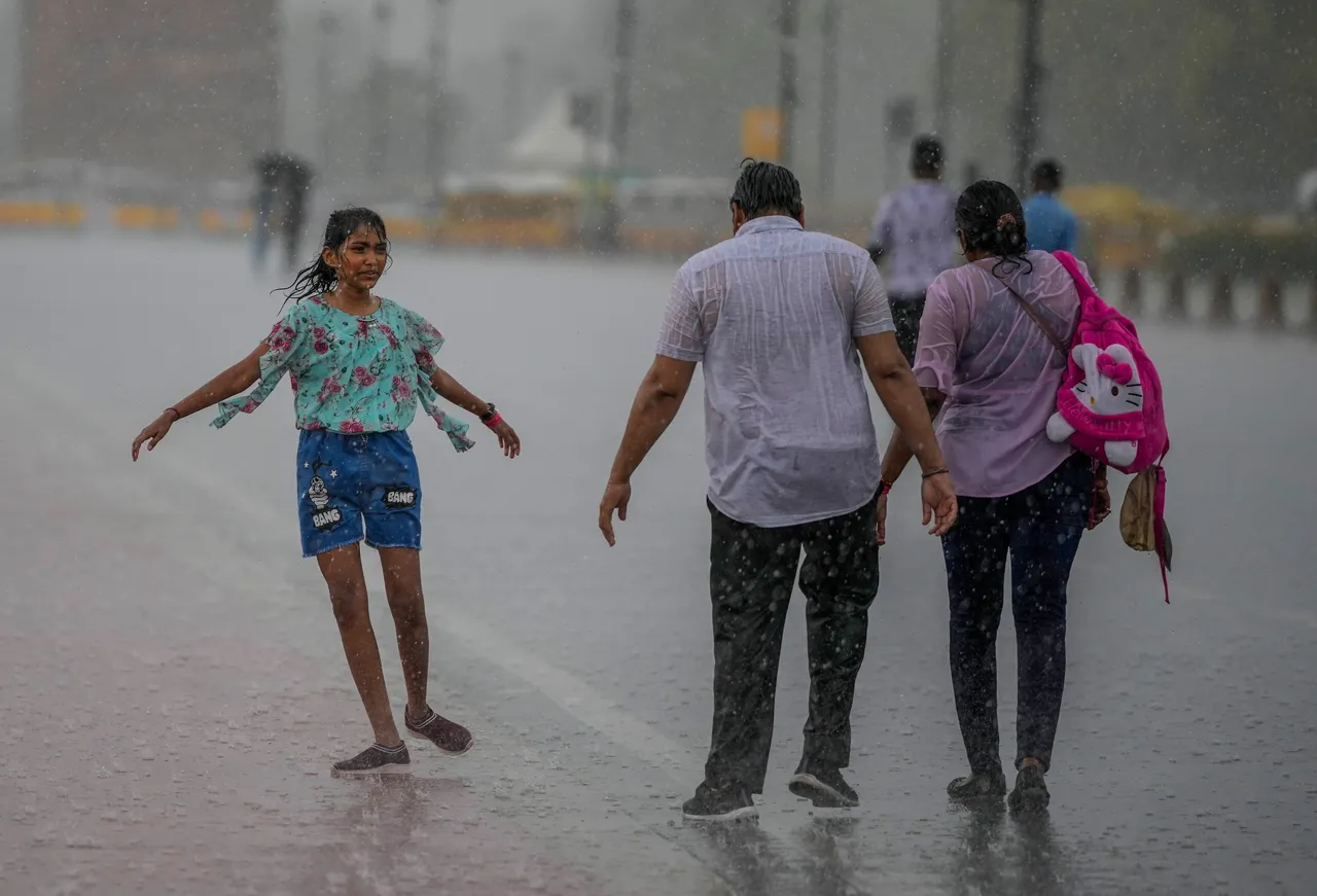 Pedestrians walk down a road during rainfall, in New Delhi