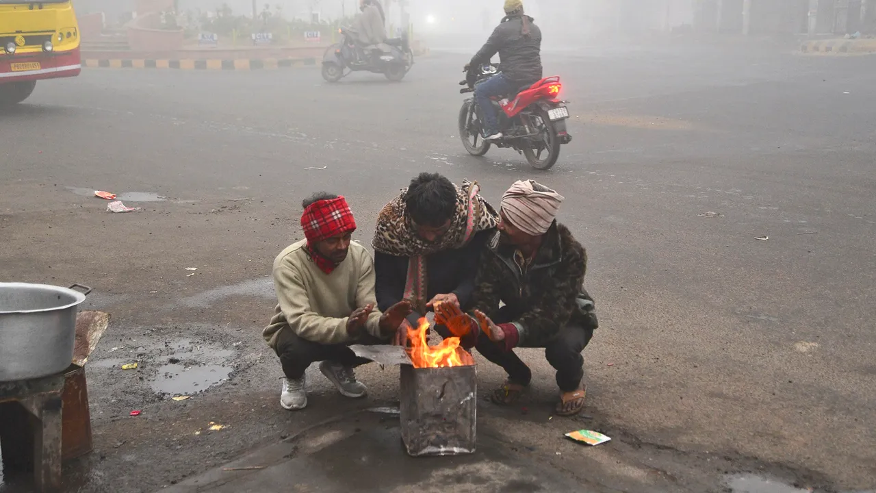 People sit around a bonfire during fog on a cold winter morning, in Jalandhar