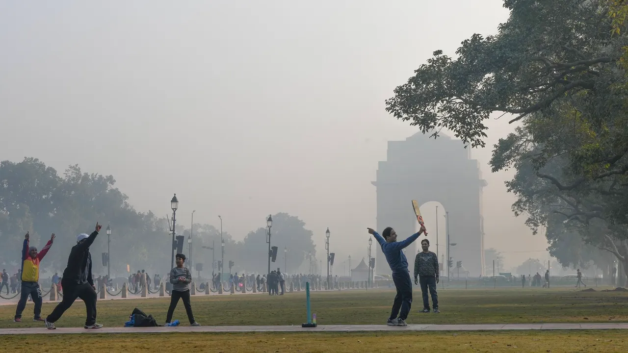 Youngsters play cricket at the lawn along the Kartavya Path during a cold and foggy winter morning, in New Delhi