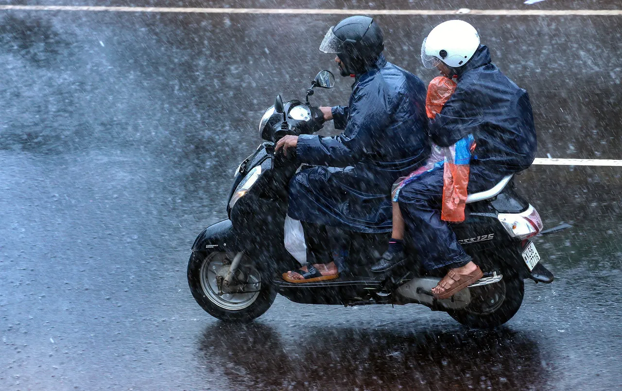 People ride past on a two-wheeler during rainfall, in Kozhikode