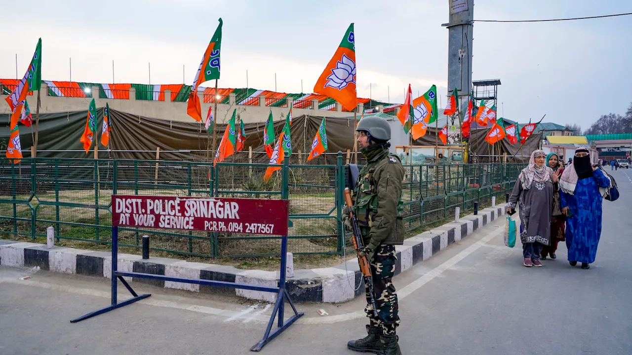Security personnel stand guard near BJP flags put up along a road ahead of Prime Minister Narendra Modi's visit to Kashmir valley, in Srinagar