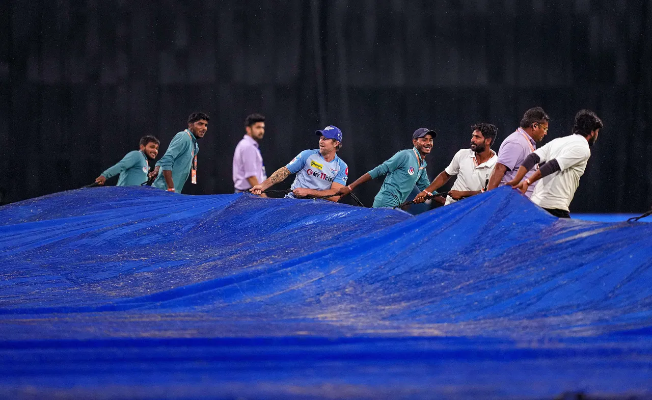 LSG coach Jonty Rhodes helps groundsmen to cover the pitch as it rains during the IPL 2023 cricket match