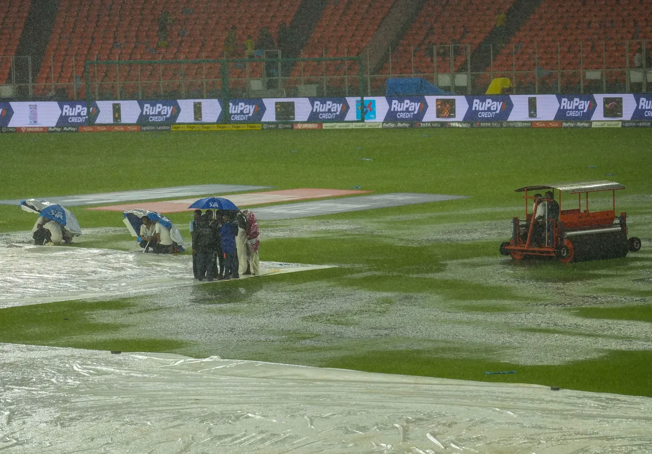 Groundsmen holding umbrellas near the covered pitch as it rains ahead of the IPL 2023 final cricket match between Gujarat Titans and Chennai Super Kings