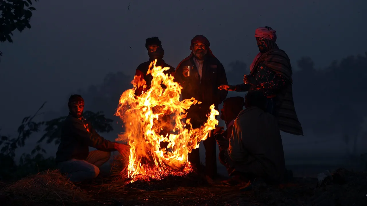 People sit around a bonfire to warm themselves during a cold and foggy winter morning, in Jammu