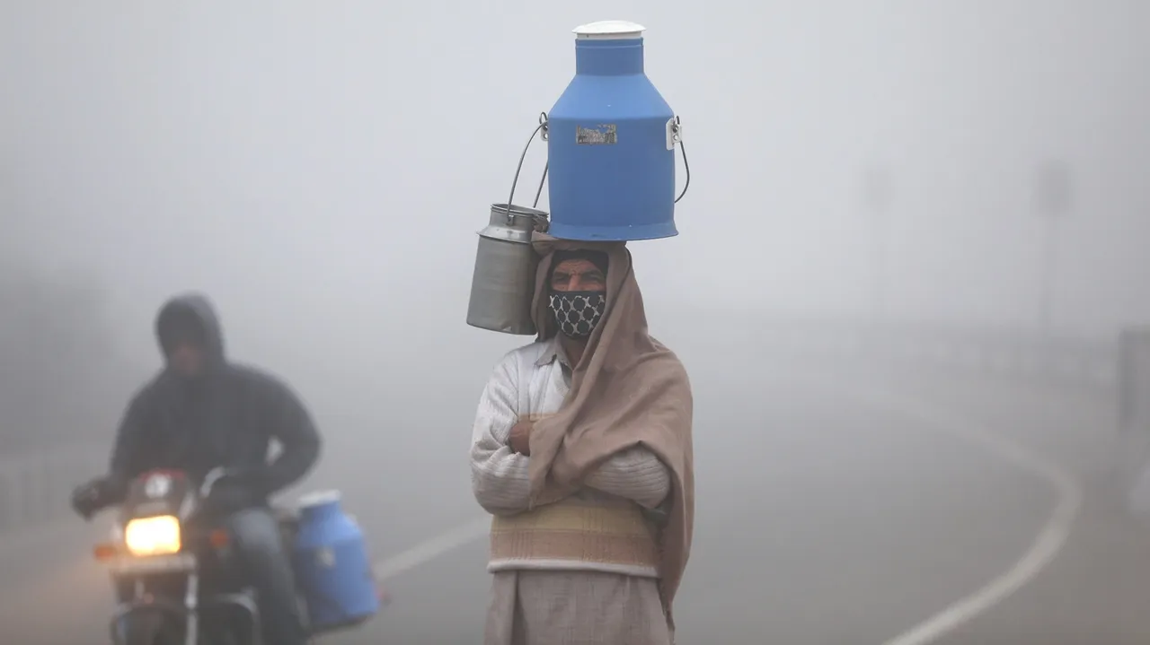 A milkman walks along the Jammu & Kashmir National Highway amid dense fog during a cold winter morning