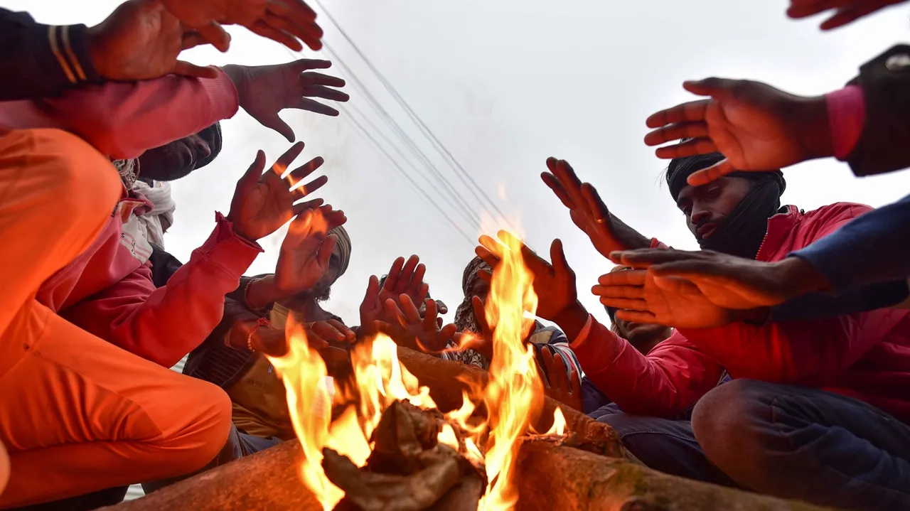 People sit around a bonefire on a cold winter day, at the Sangam in Prayagraj