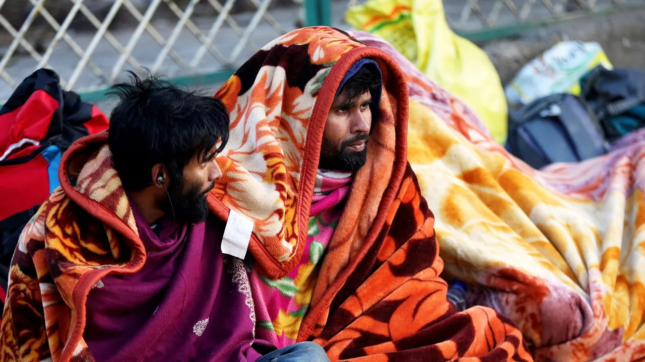 Passengers, wrapped in blankets, sit outside the Jammu railway station during a cold winter morning