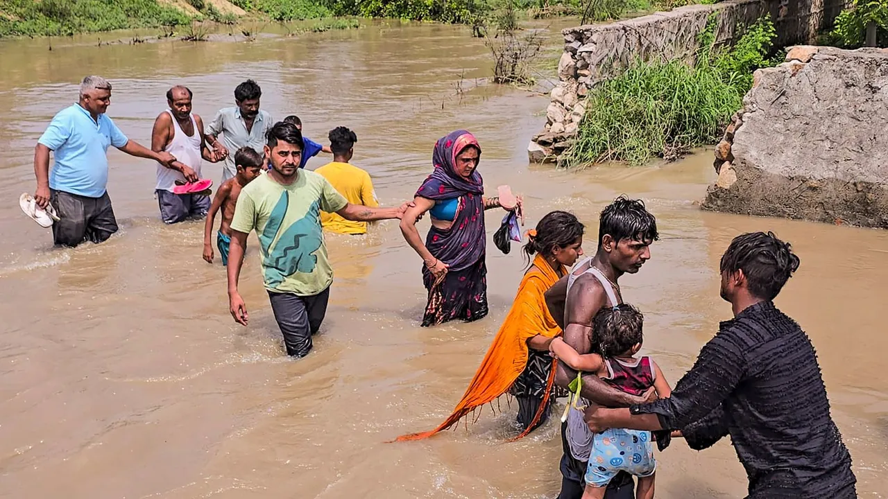 People wade through floodwater after a breach in one of the sub-branches of Munak Canal, in New Delhi, Thursday, July 11, 2024.