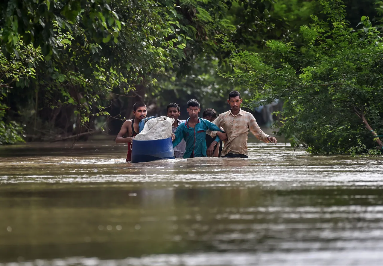 People from low-lying areas around the Yamuna river wade through floodwaters of the swollen river while relocating to a safer place, in New Delhi