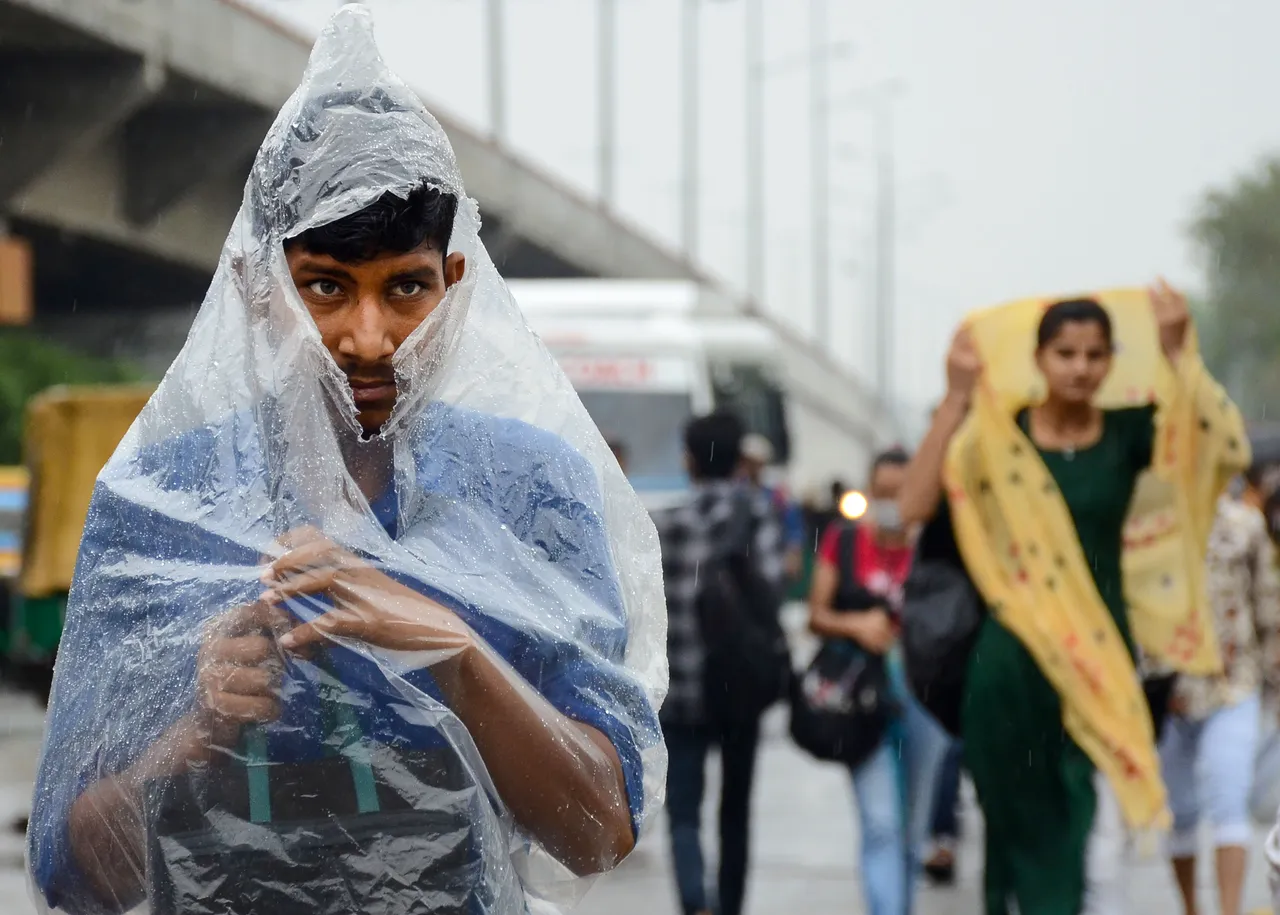 A young man covers himself with a polybag during rain, in Gurugram