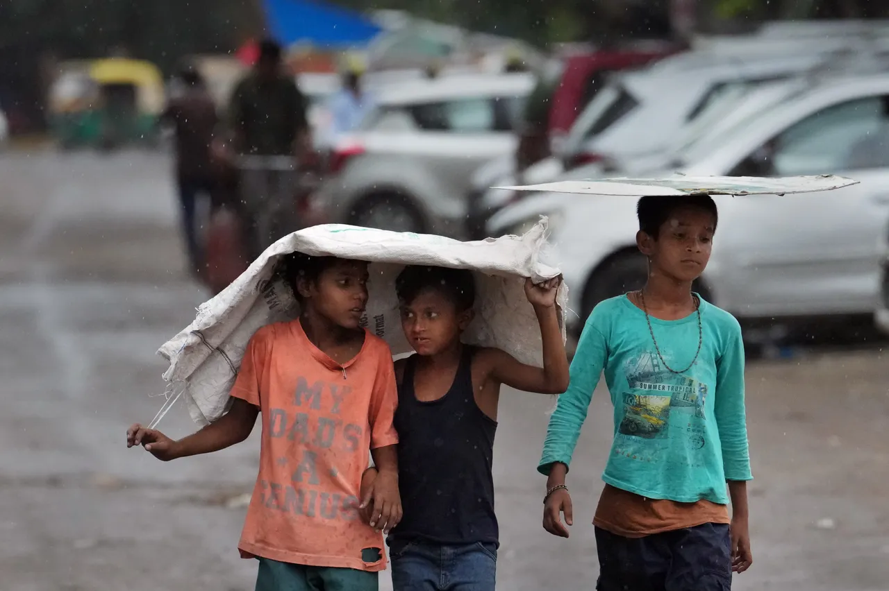 Children covering their head walk on a road during rains, in New Delhi