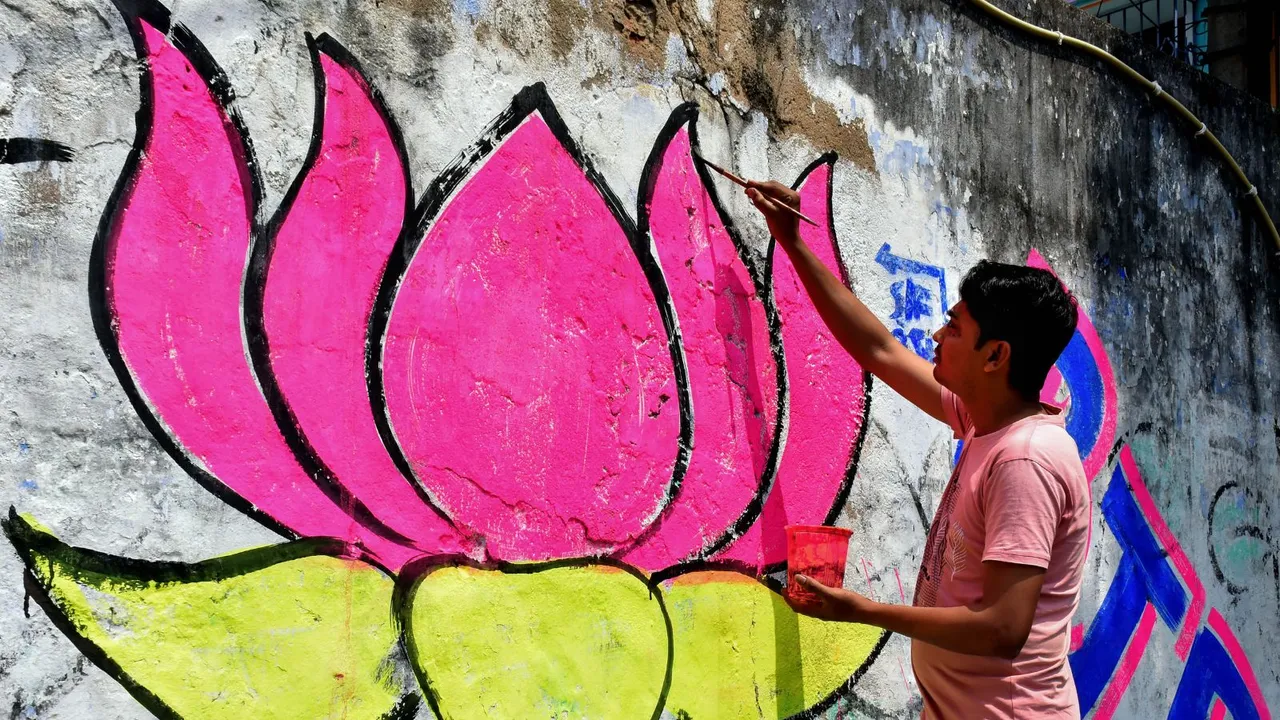 A worker paints BJP's symbol on a wall in preparation of campaigns for the upcoming General Elections 2024, in Murshidabad district