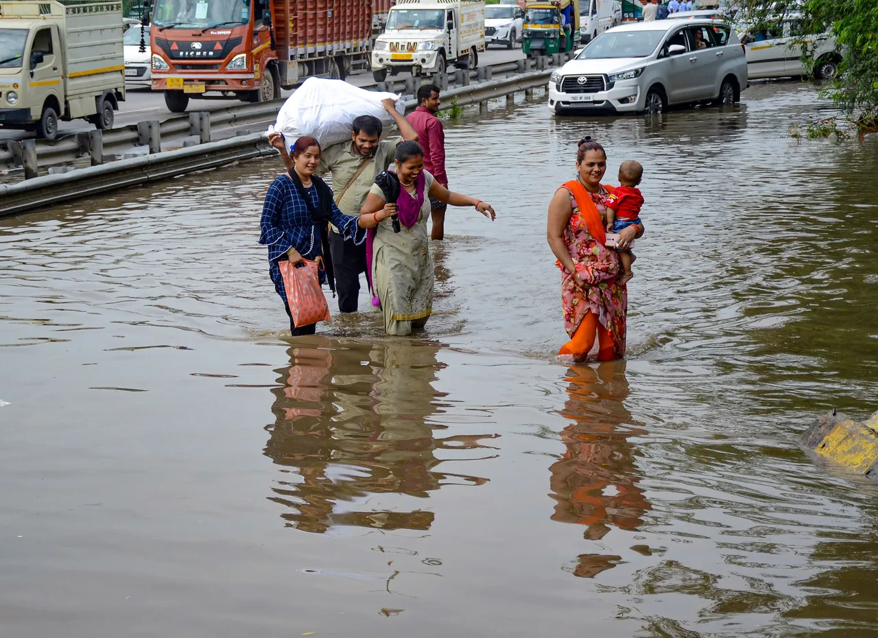 Commuters wade through waterlogged service road of the Delhi-Gurugram Expressway after heavy rainfall during the onset of monsoon, in Gurugram
