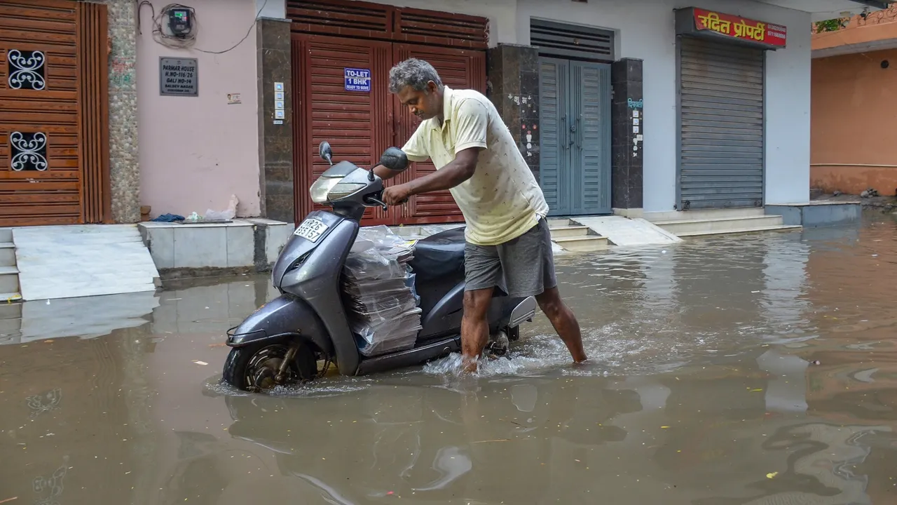 A commuter wades through a waterlogged street after monsoon rain, in Gurugram