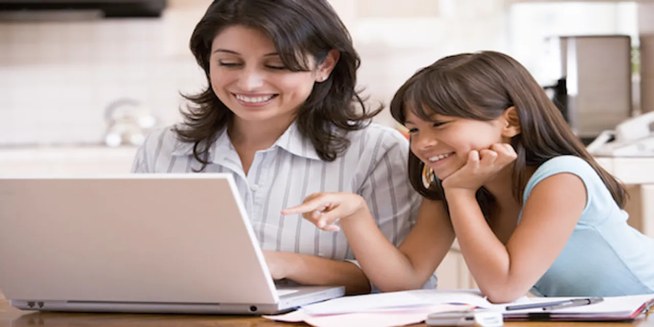 Woman and young girl in kitchen with laptop and paperwork smilin