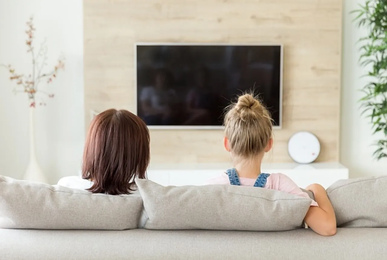Two women sitting on a couch, engrossed in watching television together.