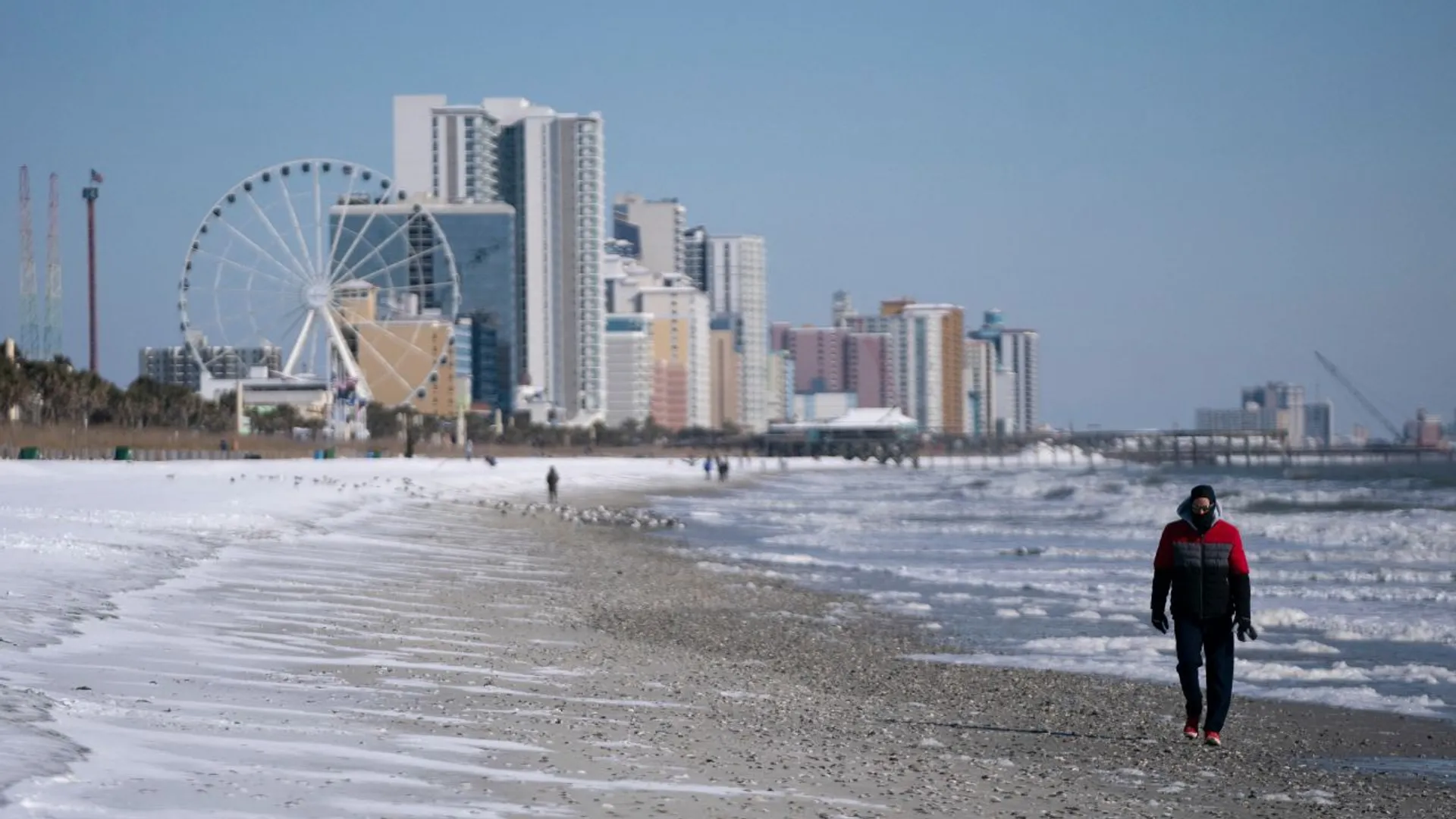 A man walks along the snow covered beach on January 22, 2025 in Myrtle Beach, South Carolina.
