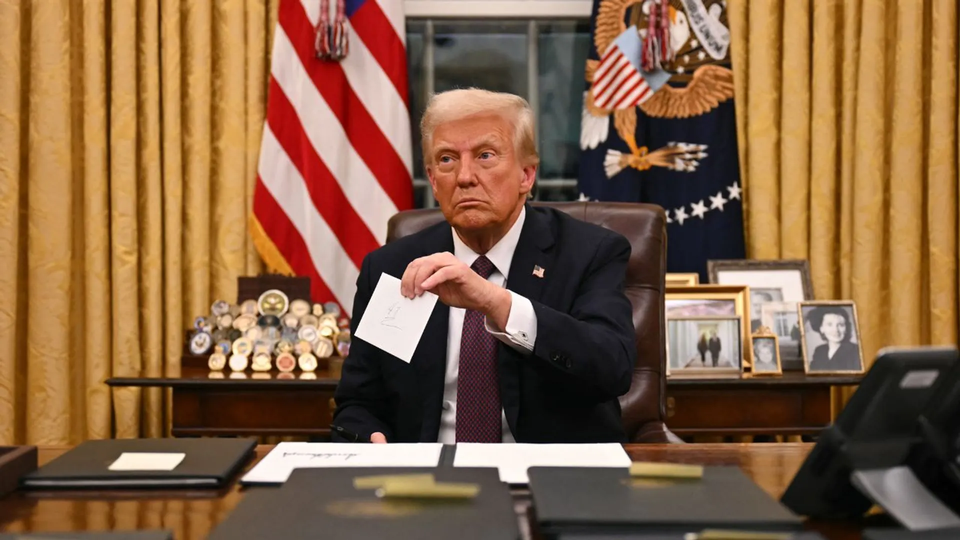 US President Donald Trump holds up outgoing President Joe Biden's letter as he signs executive orders in the Oval Office of the WHite House in Washington, DC, on January 20, 2025.