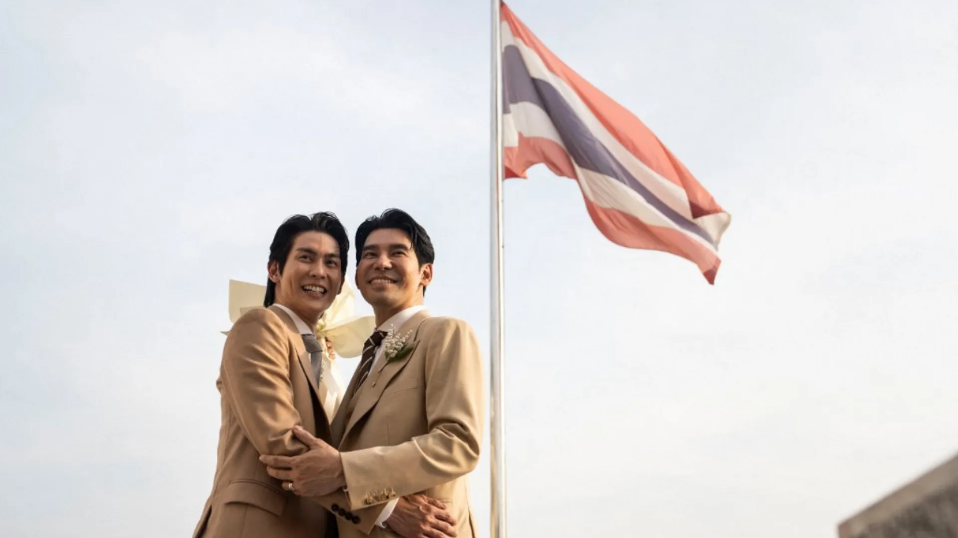 Thai actors Apiwat 'Porsch' Apiwatsayree (R) and Sappanyoo 'Arm' Panatkool pose for pictures in front of a Thai national flag after registering their same-sex marriage at the Phra Nakhon district office in Bangkok on January 23, 2025.