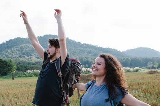 positive couple of tourists on grassy meadow with raised arms