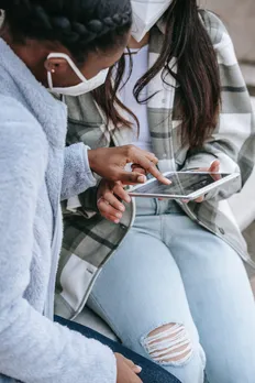 faceless multiracial female friends in masks sitting in street