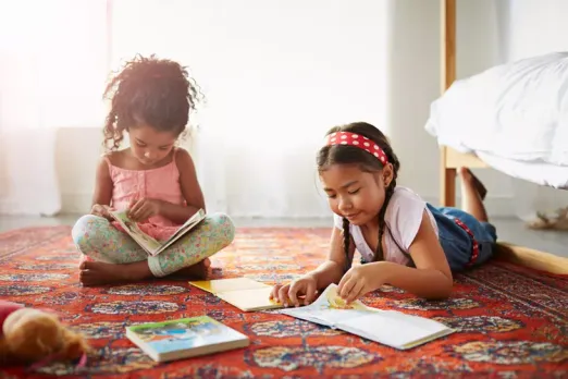 An image of two girls reading books on the floor.