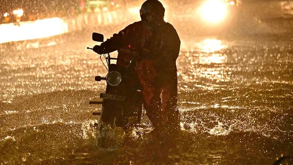 A man with his stalled vehicle wades through a waterlogged road during heavy rainfall in Bengaluru on June 2, 2024