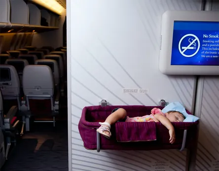 A toddler asleep in a bassinet on a plane, with leg and arm sticking over the edge