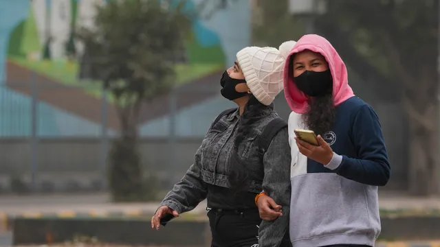 Youngsters wearing warm clothes walk down a road during a cold winter day, in New Delhi