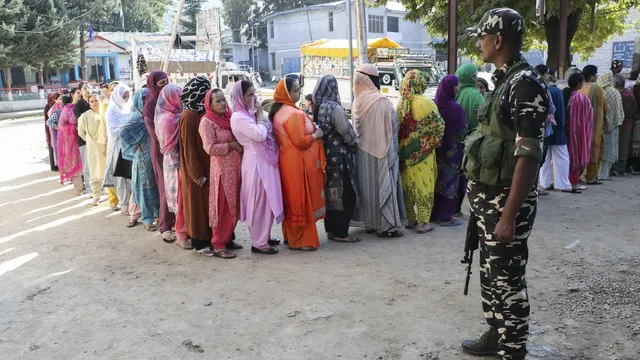 A security official stands guard as voters stand in a queue to cast votes during the first phase of Jammu and Kashmir Assembly elections, in Kishtwar district, Wednesday, Sept. 18, 2024