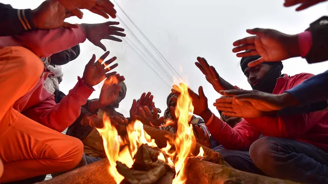 People sit around a bonefire on a cold winter day, at the Sangam in Prayagraj