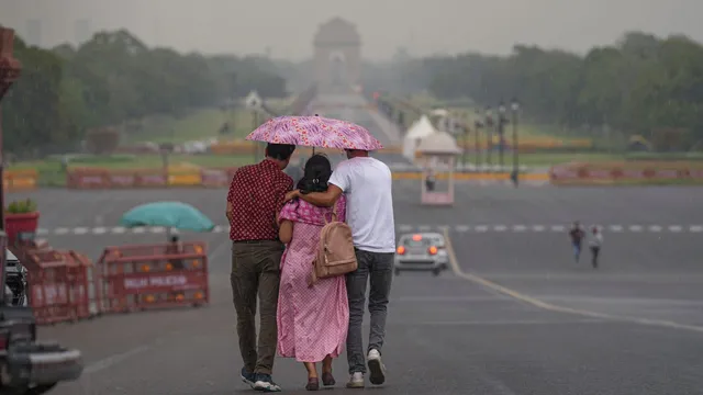 Three people share an umbrella as they walk down the Kartavya Path amid rains, in New Delhi, Friday, June 21, 2024.