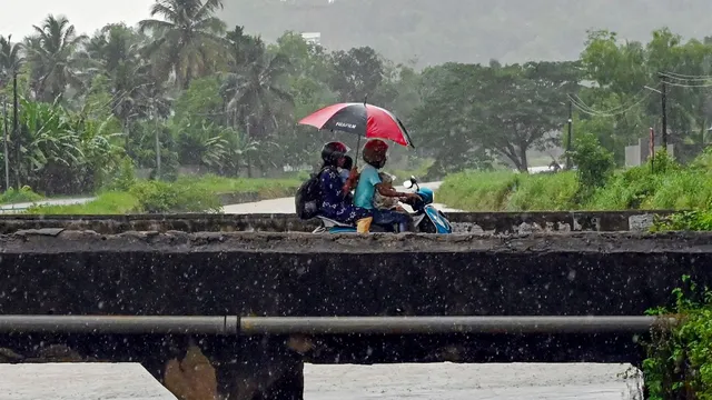 Commuters use an umbrella while riding a two-wheeler to shield themselves from the rain, ahead of monsoon, in Thiruvananthapuram, Tuesday, May 28, 2024