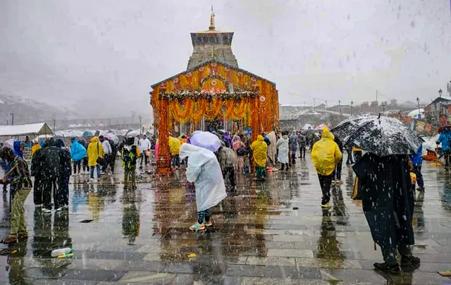 Devotees try to protect themselves as it snows at the Kedarnath temple in Rudraprayag district