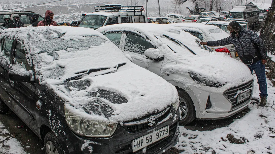 A man removes snow from vehicles after fresh snowfall, in Manali, Himachal Pradesh