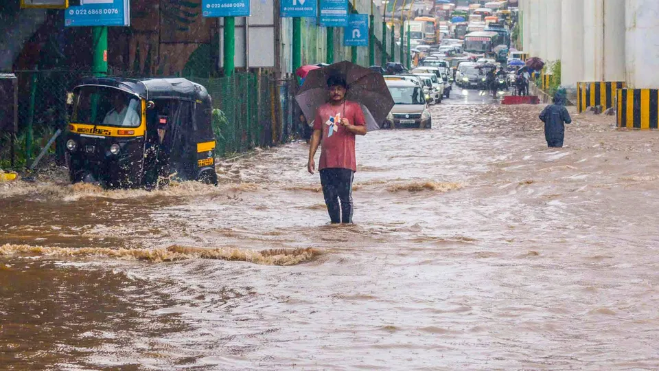 Commuters wade through a waterlogged road during rains, in Thane, Thursday, July 25, 2024.