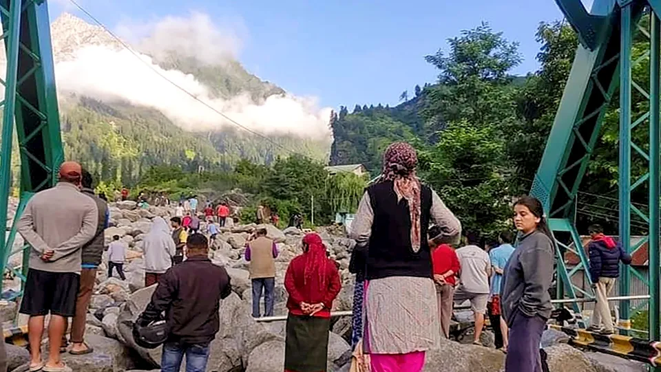 People stand near debris after flash floods triggered by cloud burst, near Manali, Thursday, July 25, 2024.