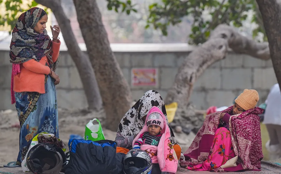 People wearing warm clothes sit at the roadside on a cold winter day, in New Delhi